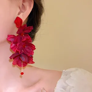 Close-up detail of elegant red fabric flower tassel earrings being worn on a model's ear