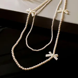 Élégant collier de perles synthétiques à deux rangs avec de délicats nœuds blancs en gros plan