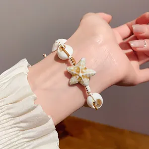 Detailed close-up of a resort style starfish and shell bracelet on a wrist with white sleeve.