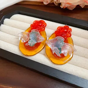 Close-up of resin koi fish and rose earrings on a white jewelry display tray.