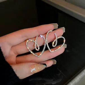Dettaglio di orecchini a cuore con strass scintillanti tenuti in mano con manicure raffinata