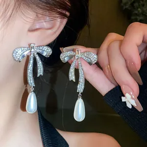 Dettaglio di orecchini a fiocco con strass e bellissime perle a goccia bianche.