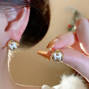 Elegant gold-tone round stud earrings with white H logo detail and silver needles.