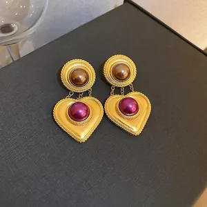 Nahaufnahme von Vintage-Herzohrringen mit lila und braunen Perlen auf dunklem Grund.