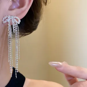 Close-up view of elegant zircon bow tassel earrings with silver pins worn on model ear.