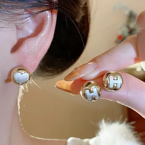 Detailed close-up of minimalist gold stud earrings featuring H-letter and heart motifs