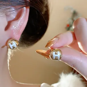 Close-up detail of golden round stud earrings with white H logo, minimalist fashion jewelry