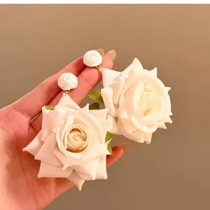 Primer plano de elegantes pendientes de rosa de tela blanca con detalles de rafia fina
