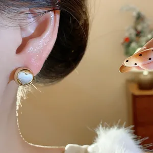 Close-up of a minimalist round gold-tone stud earring with heart inlay on ear