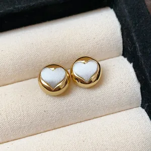 Close-up of gold circular stud earrings with elegant white heart inlay detail