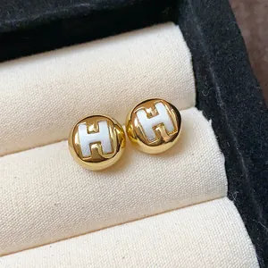 Detailed close-up of gold-plated round stud earrings featuring a white H logo design