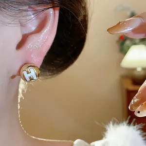 Detailed macro view of a gold circular stud earring featuring a white H logo on a model's ear