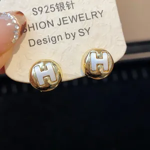 Close-up view of elegant gold round stud earrings with white H design on a jewelry card