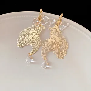 Elegant gold-plated koi fish dangle earrings with clear crystal beads on white ceramic.