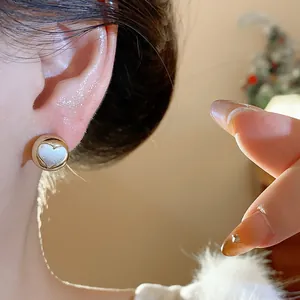 Close-up of a minimalist round gold stud earring with an elegant white heart inlay