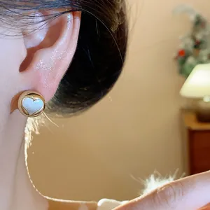 Close-up detail of minimalist gold-toned round stud earring with white heart inlay