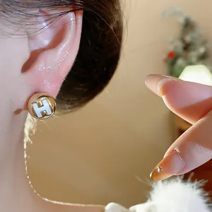 Elegant gold-plated round stud earring with a white H letter detail shown on an ear lobe