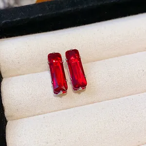 Close-up detail of elegant rectangular red zircon stud earrings on beige display cushion