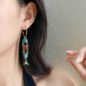 Eleganti orecchini vintage a forma di pesce smaltati indossati da una modella in primo piano.