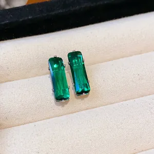 Close-up of elegant emerald green rectangular zircon stud earrings on beige tray