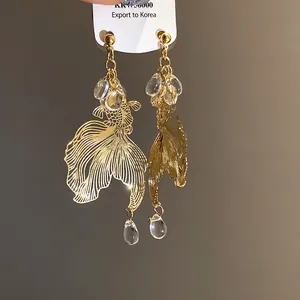 Detailed close-up of golden hollow koi fish earrings featuring clear teardrop crystal beads