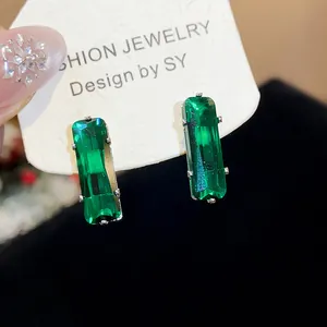 Macro view of elegant green rectangular zircon stud earrings with silver needles on card