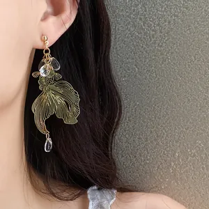 Detailed macro view of an elegant gold koi fish earring with clear crystal beads on ear.