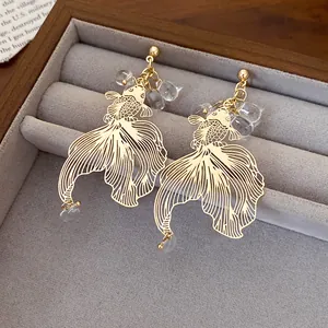 Close-up detail of golden koi fish earrings with clear beads in a gray jewelry box.