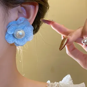 Detailed view of elegant blue mesh flower earrings with central pearl on an ear