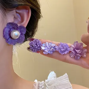 Close-up of purple floral earrings with pearl and beaded details worn by a model