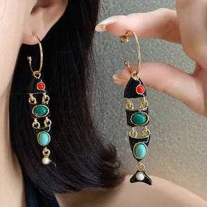 Primo piano di orecchini vintage a forma di pesce in smalto nero con pietre colorate