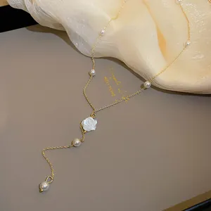 Detailed macro shot of the white rose pendant and pearl accents on the gold Y-necklace.