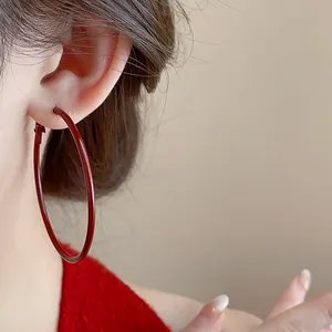 Dettaglio di un grande orecchino a cerchio rosso su modella con texture liscia