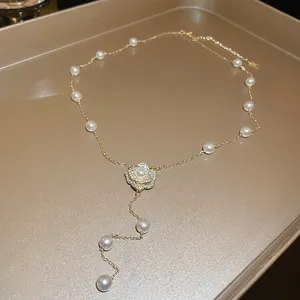 Macro view of a pearl necklace with a diamond-studded camellia flower pendant on a gold tray