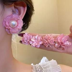 Detail view of sweet pink pearl and floral earrings worn on ear and held on hand