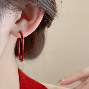 Dettaglio macro di un orecchino a cerchio laccato rosso su una modella femminile