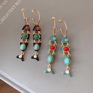 Dettaglio di orecchini pendenti vintage in smalto a forma di pesce neri e verde acqua.