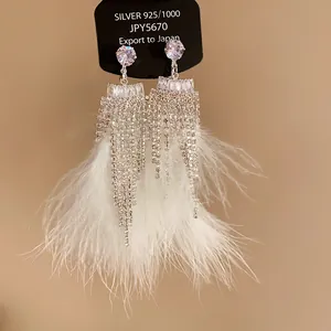 Detail of elegant silver needle earrings featuring shimmering zircon tassels and soft white feathers
