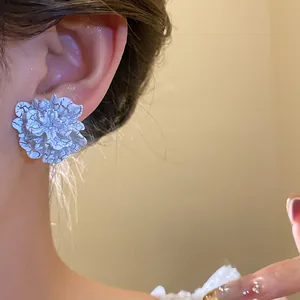 Close-up of a white flower-shaped stud earring with unique cracked texture on a model's ear.