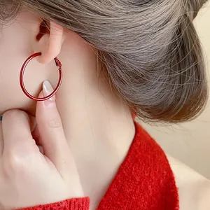Primo piano di orecchini a cerchio rossi indossati da una modella con maglione rosso