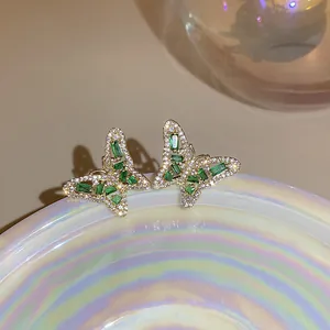 Nahaufnahme von goldenen Schmetterlingsohrringen im Vintage-Stil mit grünen Kristallen