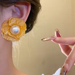 Close-up of a yellow mesh flower earring with a large pearl center worn on an ear.