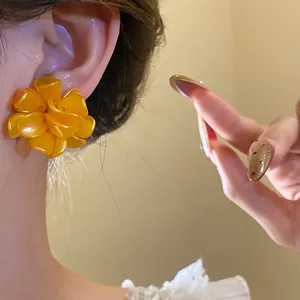 Detailed close-up shot of a vibrant yellow resin flower stud earring worn on ear