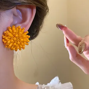 Close-up detail of a vibrant orange beaded flower stud earring worn on a model ear