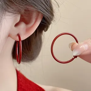 Dettaglio dei grandi orecchini a cerchio rossi indossati sull'orecchio e tenuti in mano