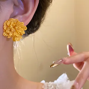Close-up of a golden textured flower earring with vintage crackle finish worn on an ear