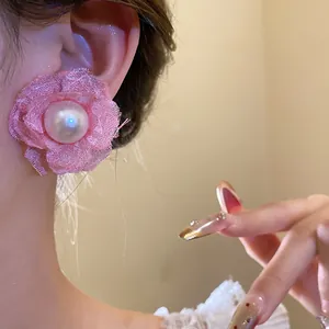 Close-up view of a delicate pink mesh flower stud earring featuring a large central pearl