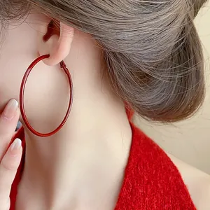 Dettaglio di un grande orecchino a cerchio rosso su una modella asiatica in rosso.