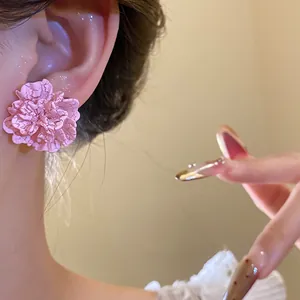 Close-up view of a pink textured flower earring with silver needle worn by a model
