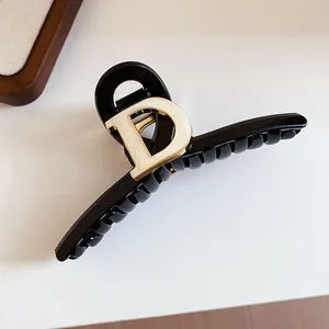Detail of elegant black hair claw clip featuring a prominent gold-toned D emblem design